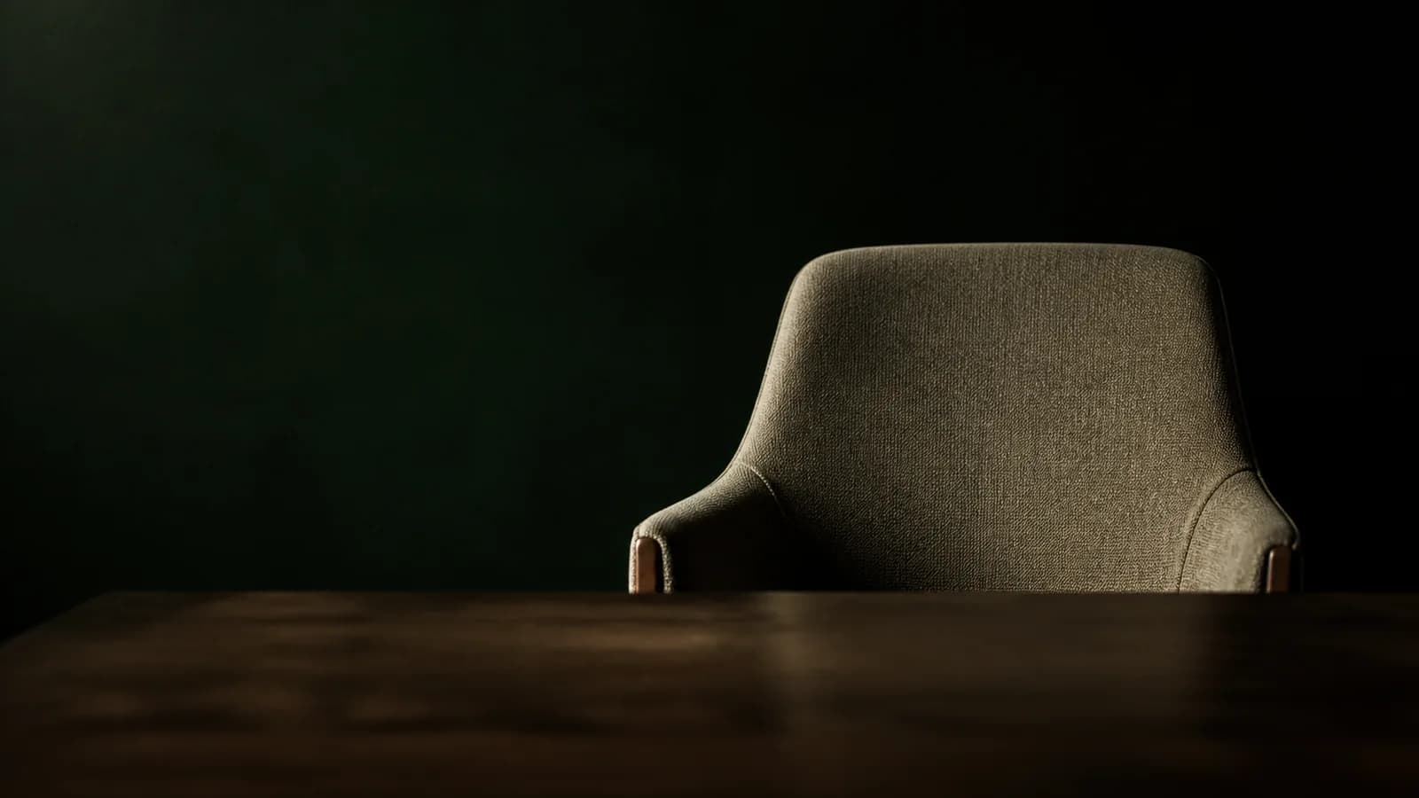 An empty chair across a dark table, seen from the interviewer's side